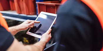 Two men wearing high visibility jackets viewing a digital tablet device in a factory environment