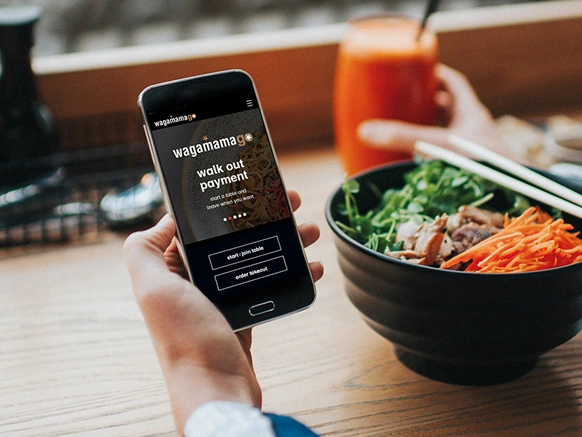 Customer holding a mobile device showing wagamamago app on screen in a wagamama restaurant venue