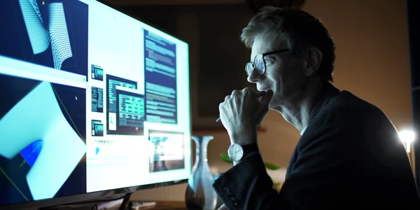 Middle-aged industry professional seated at desk viewing a monitor in a darkened office space