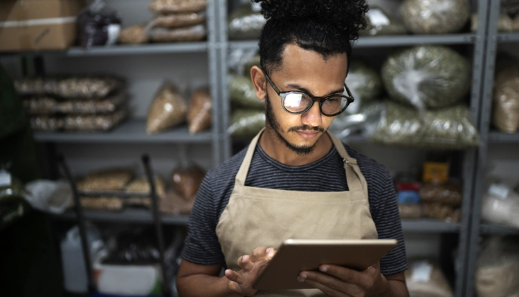 Young hospitality professional standing in a dimly lit stock area using a digital tablet device