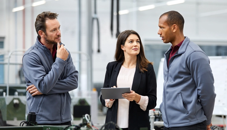 Three professional services specialists standing in a factory environment while in conversation