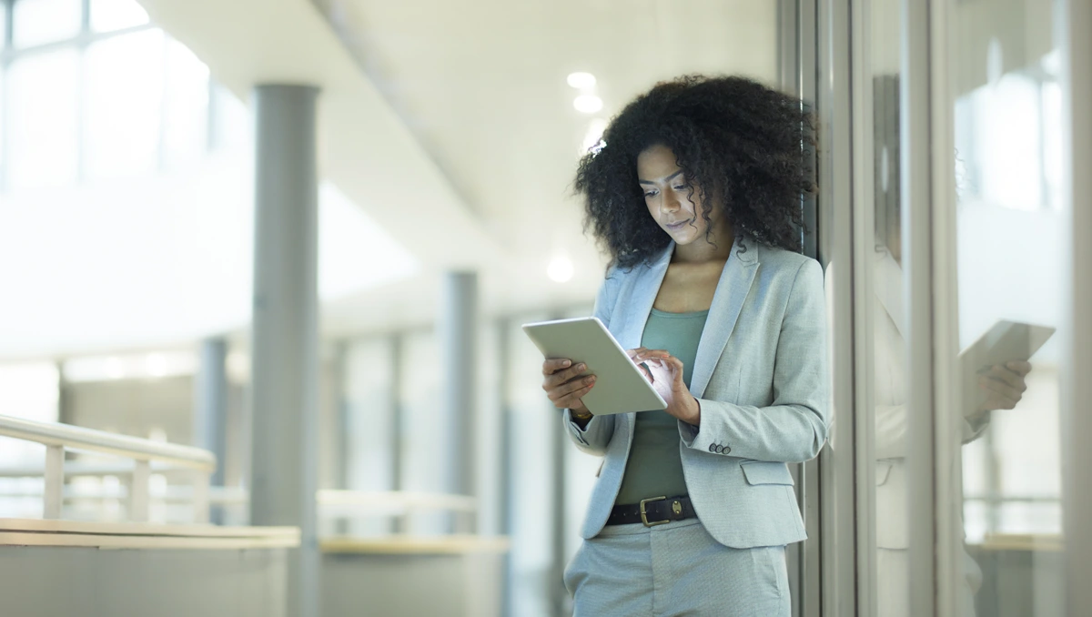 Young business professional leaning against pillar in office environment viewing a digital tablet device