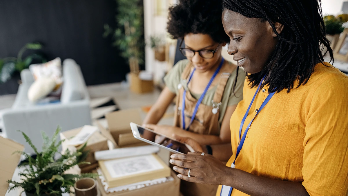 Two charity workers surrounded by parcels inspecting a digital tablet device