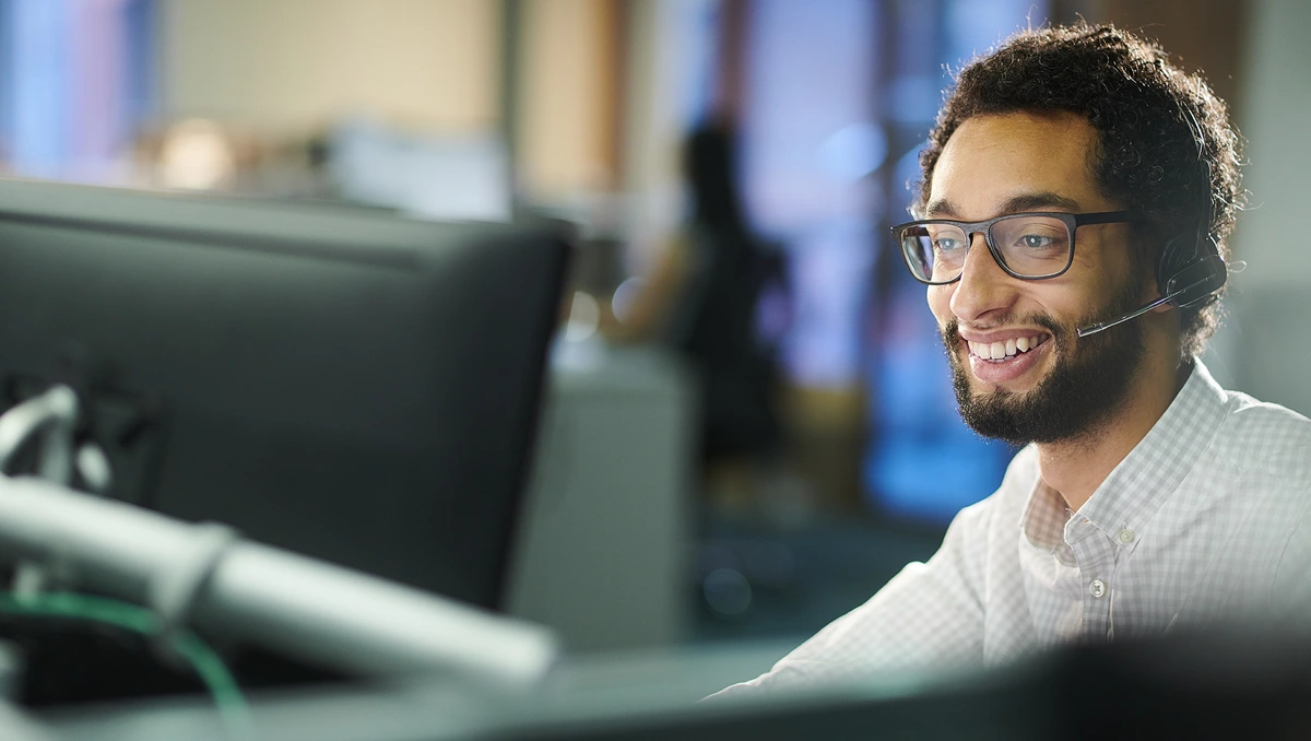 Young IT professional using a headset while viewing a computer display at his desk